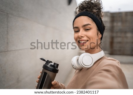 One young woman with headphones prepare for training hold supplement shaker bottle to drink water stand outdoor beautiful sporty caucasian female selfie healthy lifestyle UGC User generated content Royalty-Free Stock Photo #2382401117