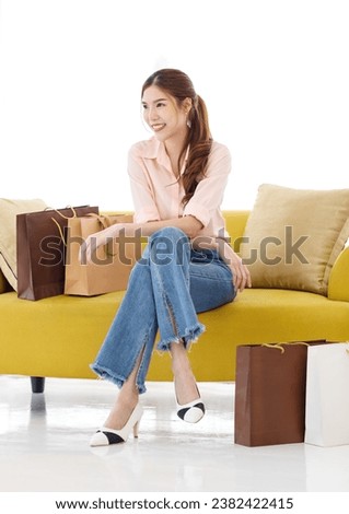 Portrait isolated cutout studio shot of Asian cheerful female client customer shopper in casual outfit sitting on cozy sofa take break buying stuff in paper shopping bags in store on white background. Royalty-Free Stock Photo #2382422415