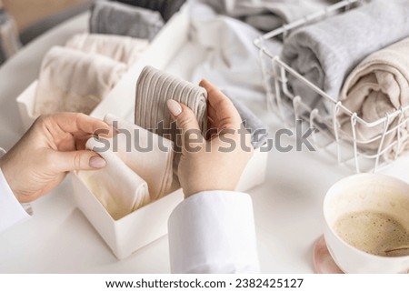 Housewife woman hands folded cotton linen domestic textile in box container and basket on table desk closeup. Female organizing comfortable storage of underwear at case. Housekeeping tidying up Royalty-Free Stock Photo #2382425127