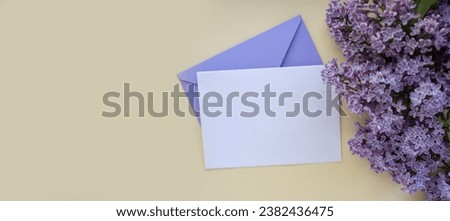 Composition with empty violet envelope and beautiful spring lilac flowers on beige background. Mockup card invitation greeting card postcard copy space template. Branches of lilac blooming bouquet. 