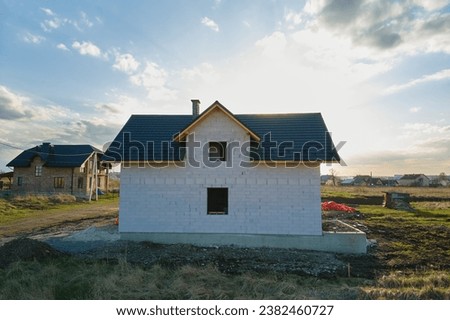 Aerial view of unfinished house with aerated lightweight concrete walls and wooden roof frame covered with metallic tiles under construction. Royalty-Free Stock Photo #2382460727