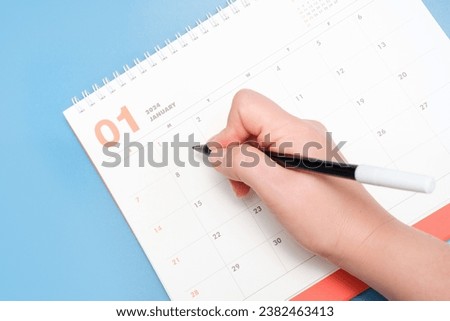Calendar for January 2024 and female hand on a blue background, planning concept. Royalty-Free Stock Photo #2382463413