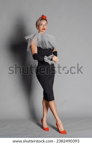 Elite clown. Woman dressed as clown iblack dress with harlequin collar and red hat. Contrast image on grey background. High quality photo