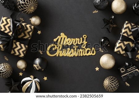 Merry Christmas greeting card. Striped gift boxes with black ribbon bow, gold and black Xmas balls ornaments and confetti on black background. Flat lay, top view.