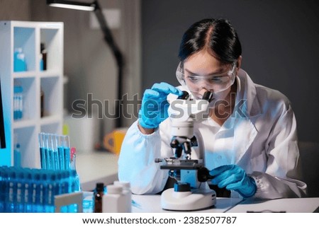 Asian female scientist looking under microscope, analyzes petri dish sample. specialists working on medicine, biotechnology research in advanced pharmacy lab, Medical development laboratory. Royalty-Free Stock Photo #2382507787