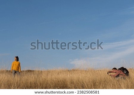 Man taking photo of a woman in the autumn field against blue sky during warm sunny day. Weekend, leisure, relationship activities concept