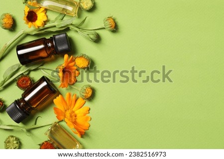 Bottles of essential oils and beautiful calendula flowers on green background, flat lay. Space for text