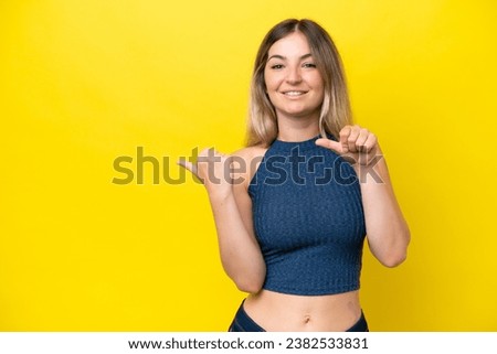 Young Rumanian woman isolated on yellow background pointing to the side to present a product