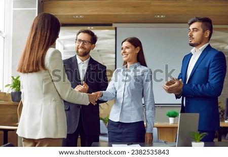 Two women shaking hands celebrating success, making a deal, business achievement or signing a contract on their workplace. Group of business people in office applauding to their coworkers.