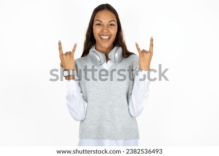 young beautiful business woman wearing formal clothes makes rock n roll sign looks self confident and cheerful enjoys cool music at party. Body language concept.