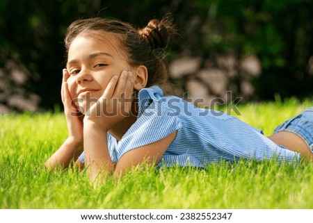 A picture of a little girl lying in the grass with her hands on her face. This image can be used to depict emotions such as surprise, sadness, or contemplation. It can also be used in concepts related