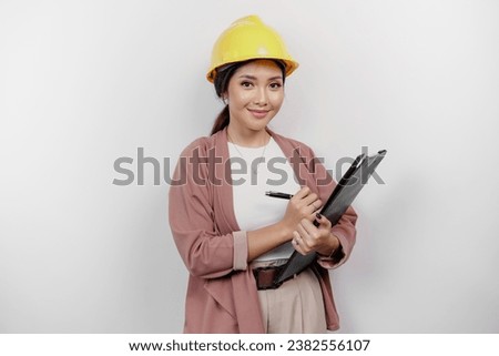 Smiling young Asian woman employee wearing safety helmet while holding a clipboard, isolated by white background