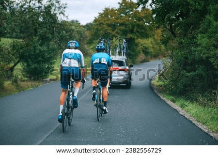 Professional cyclist race. Two cyclists behind the peloton in convoy of cars on the road. Cycling road Race, preparation for Tour race in France. Royalty-Free Stock Photo #2382556729