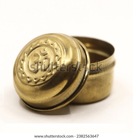 closeup of a golden bronze box jar with hindu om symbol inscribed on the crafted lid isolated in a white background Royalty-Free Stock Photo #2382563647