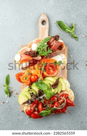 a set of bruschetta with prosciutto, salmon, tomatoes and avocado on a light background. top view