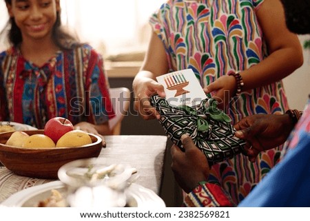 Focus on hands of girl in ethnic dress passing giftbox and kwanzaa greeting card