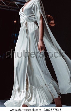 Elegant fashion details of white long silky bridal dress. Fashion model walking on black background Royalty-Free Stock Photo #2382577515