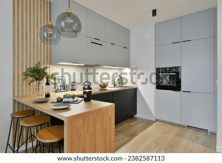 Contemporary kitchen in black and grey colours with built in appliances, wooden dining table top and decorative slats Royalty-Free Stock Photo #2382587113