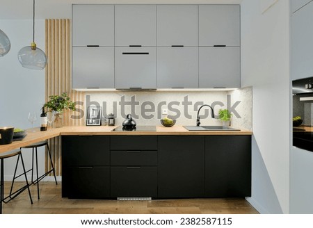 Contemporary kitchen in black and grey colours with built in appliances, wooden dining table top and decorative slats