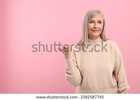 Portrait of beautiful middle aged woman pointing at something on pink background, space for text