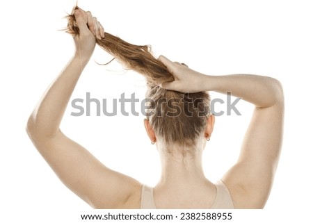 Back,  rear view of a young blond woman tying her long hair on a white studio background