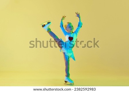 Artistic, talented little girl, child, performing figure skating in beautiful costume against yellow background in neon light. Concept of childhood, figure skating sport, hobby, school, education