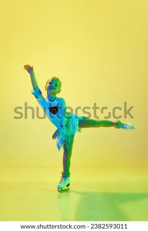 Artistic, talented little girl, child, adorable kid in costume dancing, training figure skating against yellow background in neon. Concept of childhood, figure skating sport, hobby, school, education