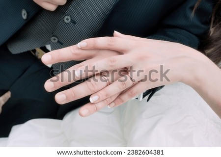 The bride's hand resting on top of the groom's hand, with the wedding rings in the foreground Royalty-Free Stock Photo #2382604381