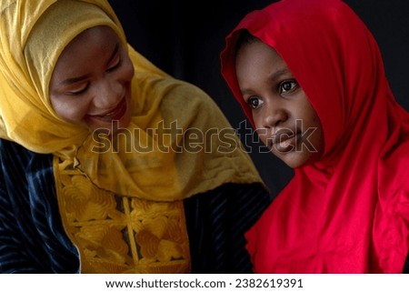 Close relationship between African Muslim mother and daughter, wear a colorful hijab on black background