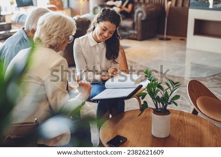 A hotel or travel agency representative is talking with a senior tourist couple offering various tourist services Royalty-Free Stock Photo #2382621609
