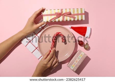 Gift boxes, plate, decorations and female hands on pink background, top view