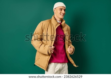 cheerful young man in beanie hat and stylish puffer jacket on turquoise background, winter trends Royalty-Free Stock Photo #2382626529