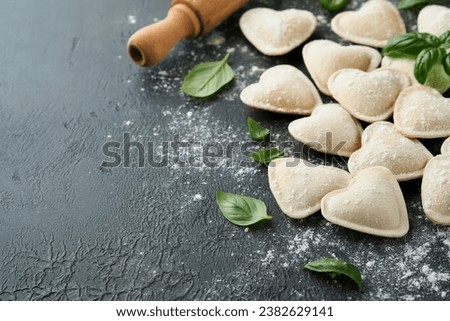 Italian ravioli pasta in heart shape. Tasty raw ravioli with flour and basil on dark background. Food cooking ingredients background. Valentines or Mothers Day lunch ideas. Top view with copy space. Royalty-Free Stock Photo #2382629141