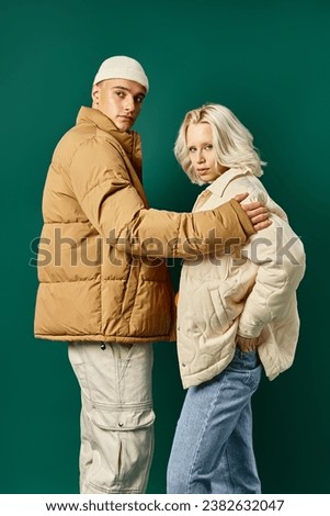 stylish couple in puffer jackets posing together on turquoise background, young man and woman Royalty-Free Stock Photo #2382632047