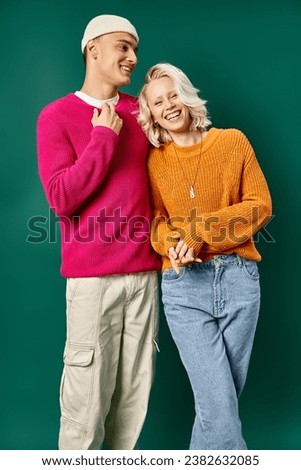 cheerful young couple in winter sweaters laughing and looking at camera on turquoise background Royalty-Free Stock Photo #2382632085