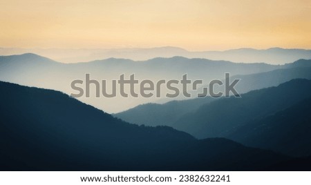 Mountain range with visible silhouettes through the morning colorful fog.Calm evening landscape in the mountains at sunset. Photo wallpaper. Natural background. Panorama. Carpathian Mountains, Ukraine