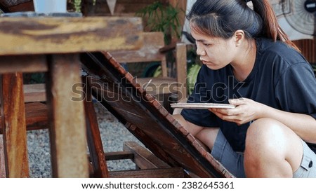 Asian woman painter creating art use a paintbrush to draw lettering designs on a wooden coffee shop sign. outdoor activities, People doing activities. 