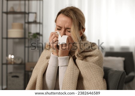 Sick woman wrapped in blanket blowing nose in tissue at home. Cold symptoms Royalty-Free Stock Photo #2382646589