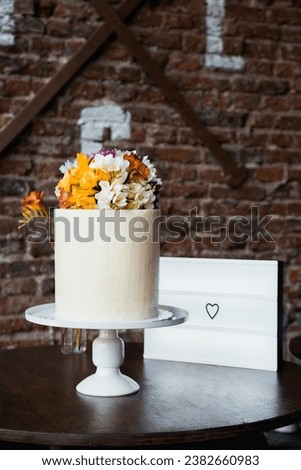 A rustic wedding cake with delicate flowers on top. Vintage and elegant style. Cinema Lightbox sign in the background with a heart. Concept of love.