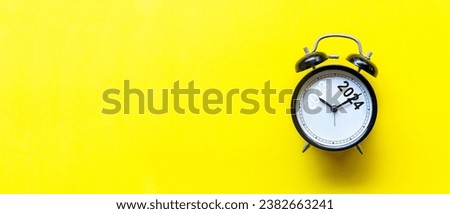 2023 and 2024 on black alarm clock on yellow background, Merry Christmas and Happy new year concept. Copy space and banner for text