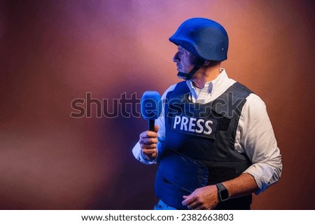 Reporter with bulletproof vest holding a microphone in studio. Royalty-Free Stock Photo #2382663803