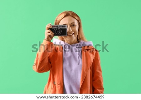 Mature woman in coat with photo camera on green background