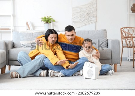 Frozen family warming near electric fan heater at home Royalty-Free Stock Photo #2382679289