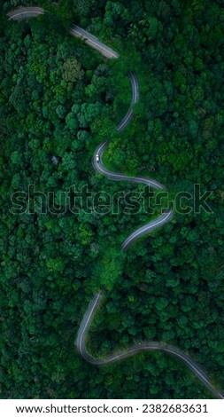 beautyfull curved road with small driving car and green forest in the rain season rural routes connecting city  north of thailand Ecosystem and ecology healthy environment concepts drone point of view
