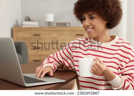 Beautiful young woman using laptop and drinking coffee at wooden table in room