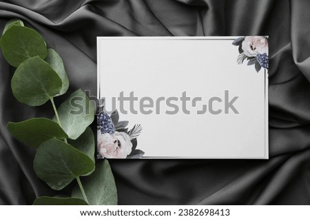 Blank invitation card and eucalyptus leaves on black fabric, flat lay