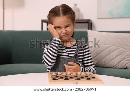 Thoughtful girl playing checkers on sofa at home
