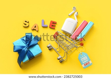 Composition with gadgets, small shopping cart and gift box on yellow background. Cyber Monday sale