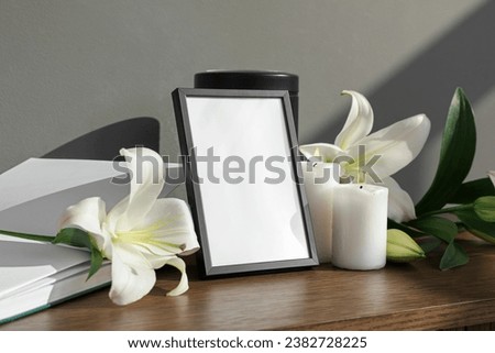 Blank funeral frame, book and white lily flowers on wooden table