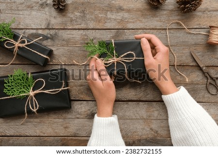 Female hands with Christmas gift boxes and coniferous branches on wooden background